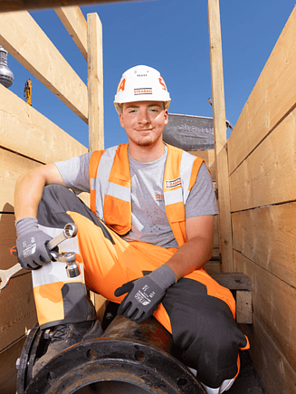 Young man wearing a hard hat, sitting on a metal pipe