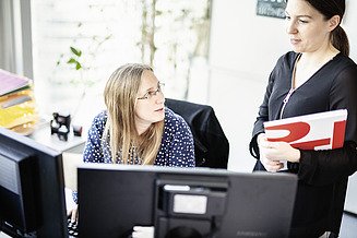 Foto Twee vrouwelijke werknemers discussiëren voor twee schermen